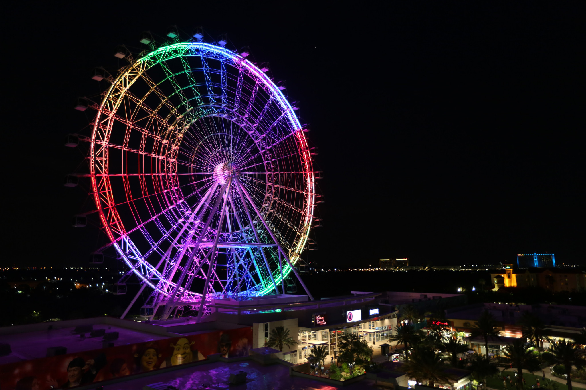 A night photo of the Coca-Cola Orlando Eye lit up in colors of the rainbow.